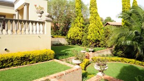 A well-maintained garden with neatly trimmed hedges, tall trees, and a variety of plants.