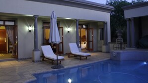 A pool area with lounge chairs and umbrellas, a covered seating area, and a pool with a tiled edge.