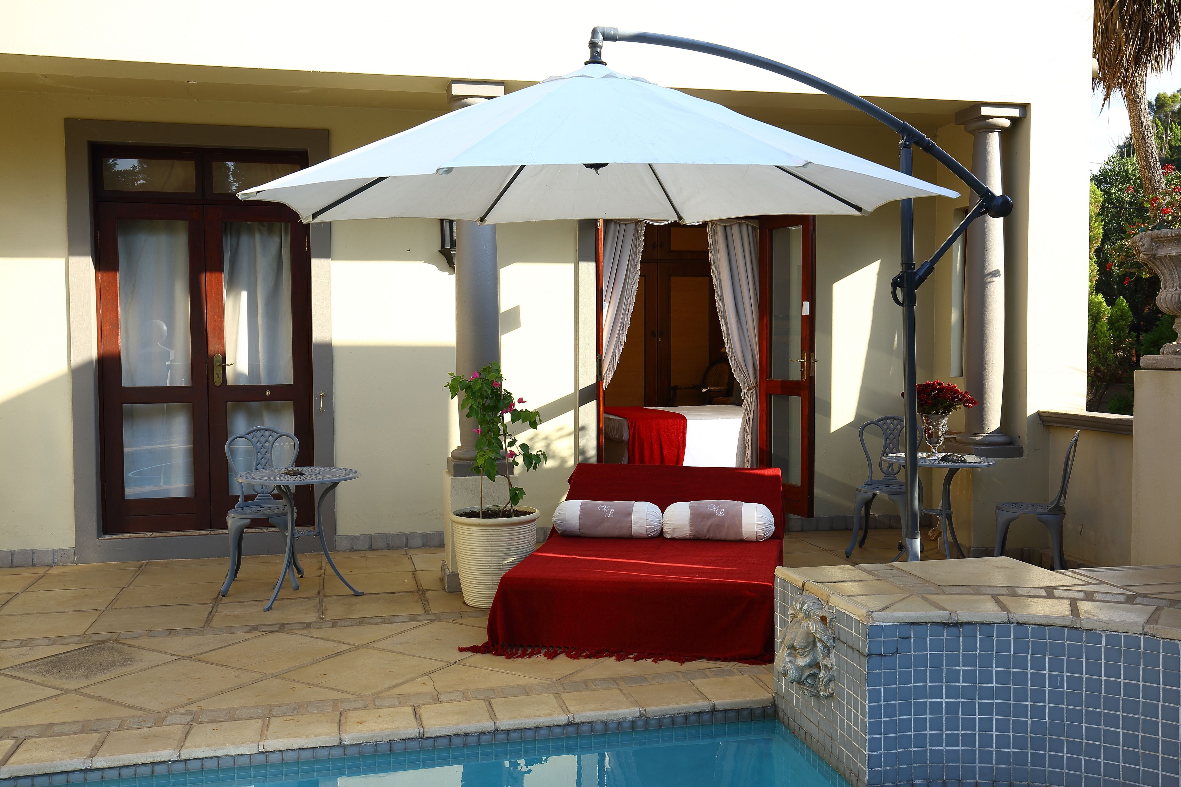 Zona junto a la piscina con un sofá rojo, una mesa y una silla bajo un paraguas grande.