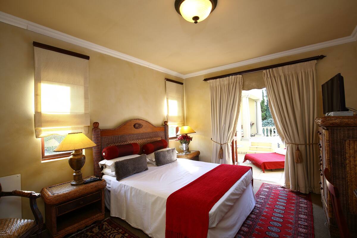 A hotel room with a large bed, a wooden nightstand, a lamp, a chair, a window with curtains, and a view of the outdoors.