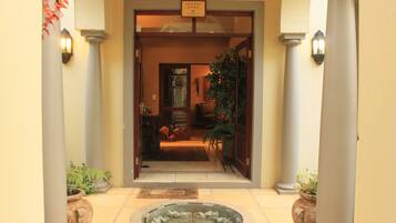 Entrada de un hotel con recepción, letrero de casa de huéspedes y plantas en macetas.