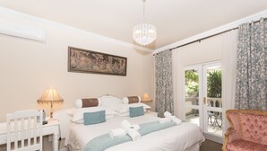 A hotel room with a bed, bedside tables, a desk, a chair, a chandelier, and a view through the glass door.