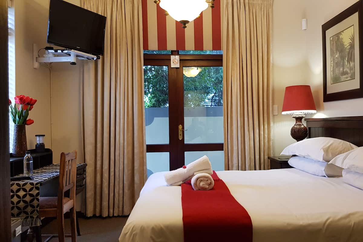 A hotel room with a bed, a desk, a chair, a TV, a lamp, and a window with curtains.