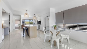 Une cuisine moderne avec des meubles blancs, un îlot central et un coin repas avec des chaises blanches.
