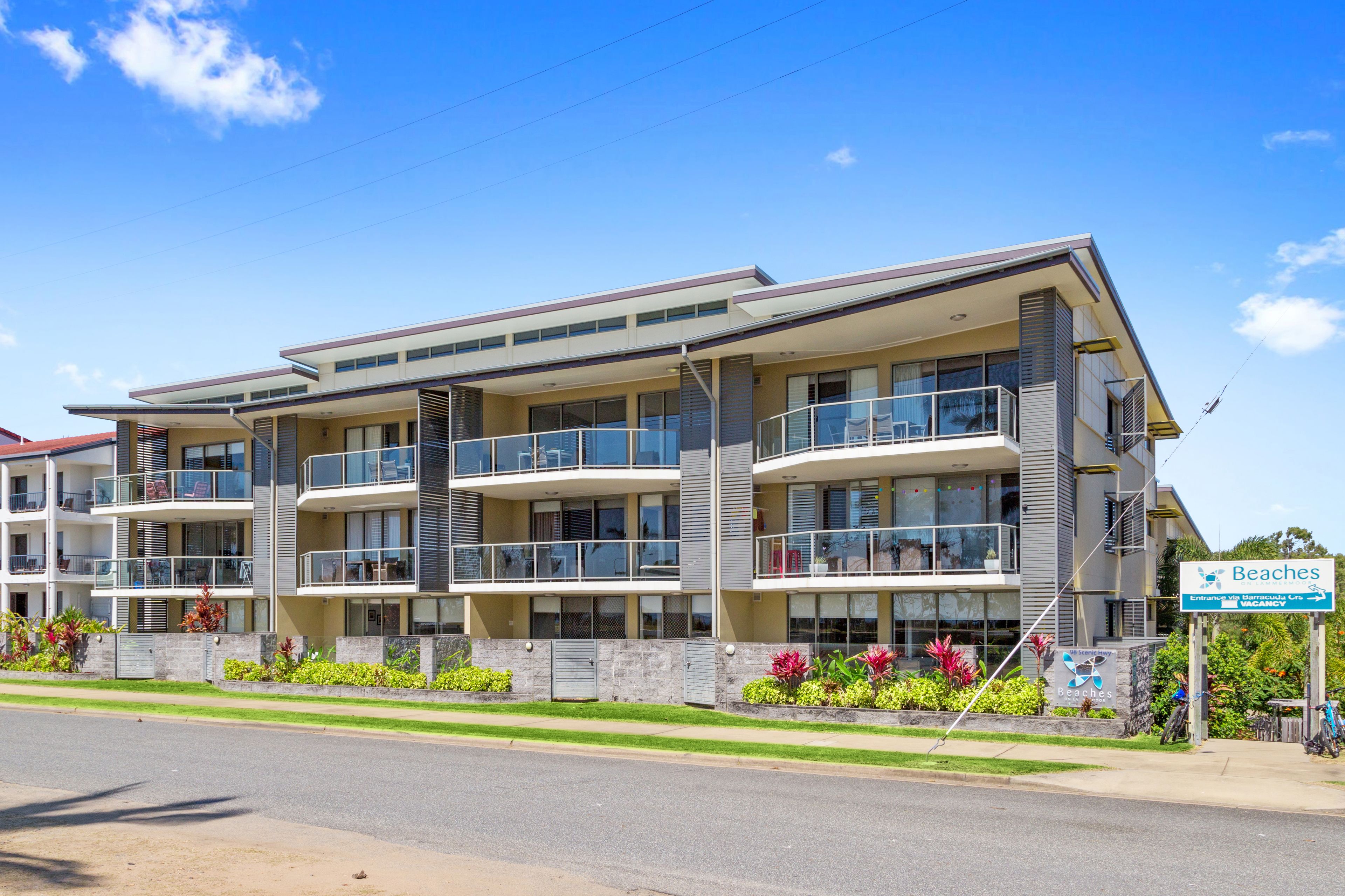 Un hôtel à plusieurs étages doté de balcons, d’un panneau indiquant l’accès à la plage et d’un jardin aménagé.