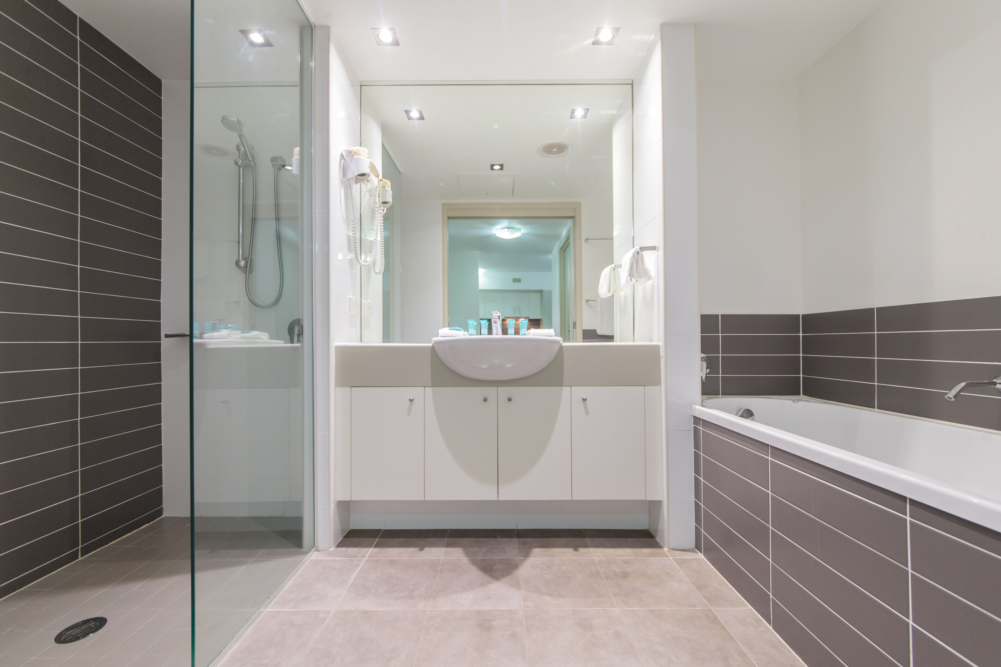 A modern bathroom with a glass-enclosed shower, a large bathtub, and a vanity with cabinets.
