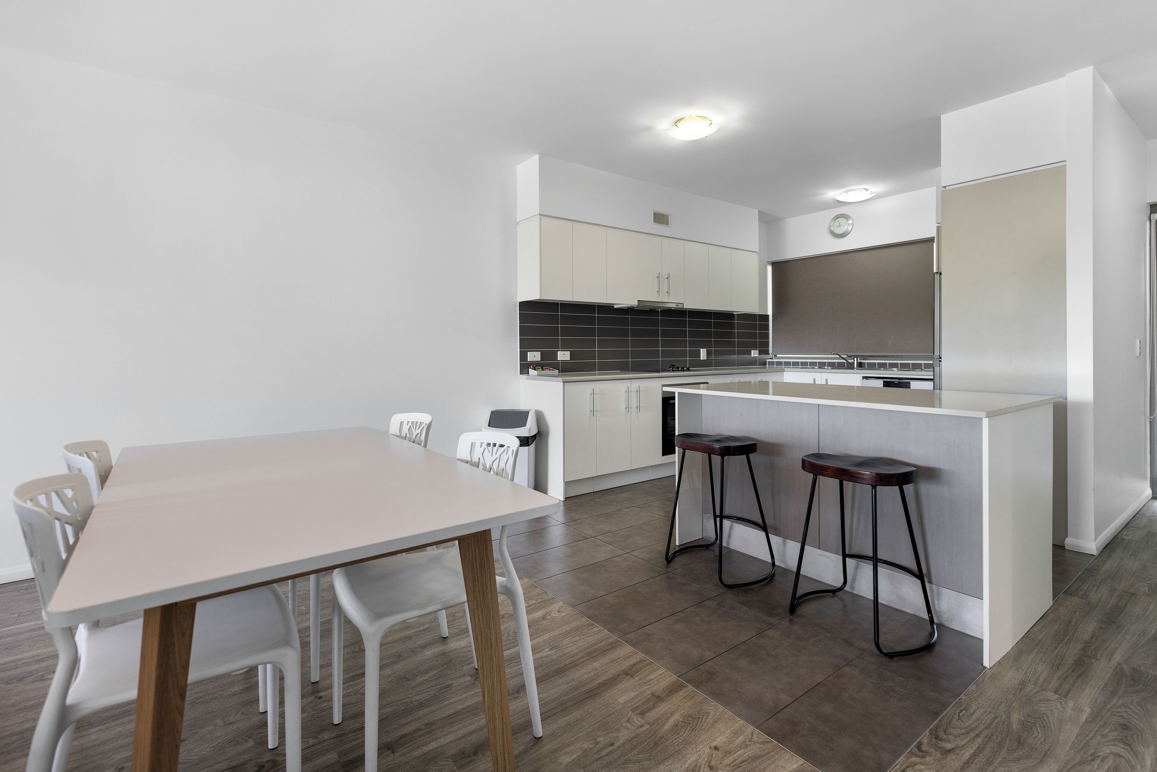 Una cocina moderna con armarios blancos, salpicadero negro y una mesa de comedor de madera con sillas blancas.