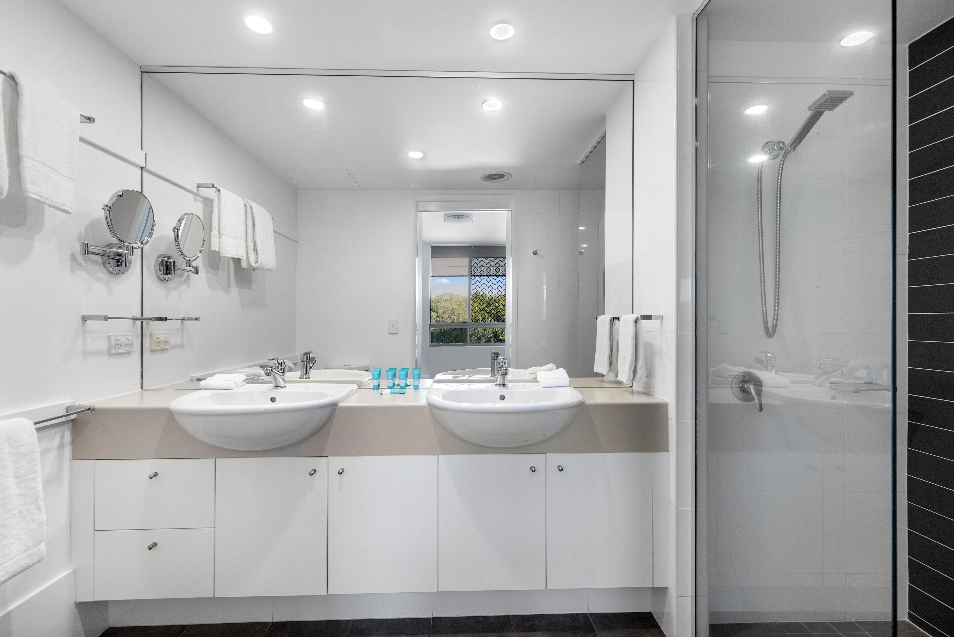 Een moderne badkamer met twee wastafels, een grote spiegel en een douchecabine met glazen wanden.