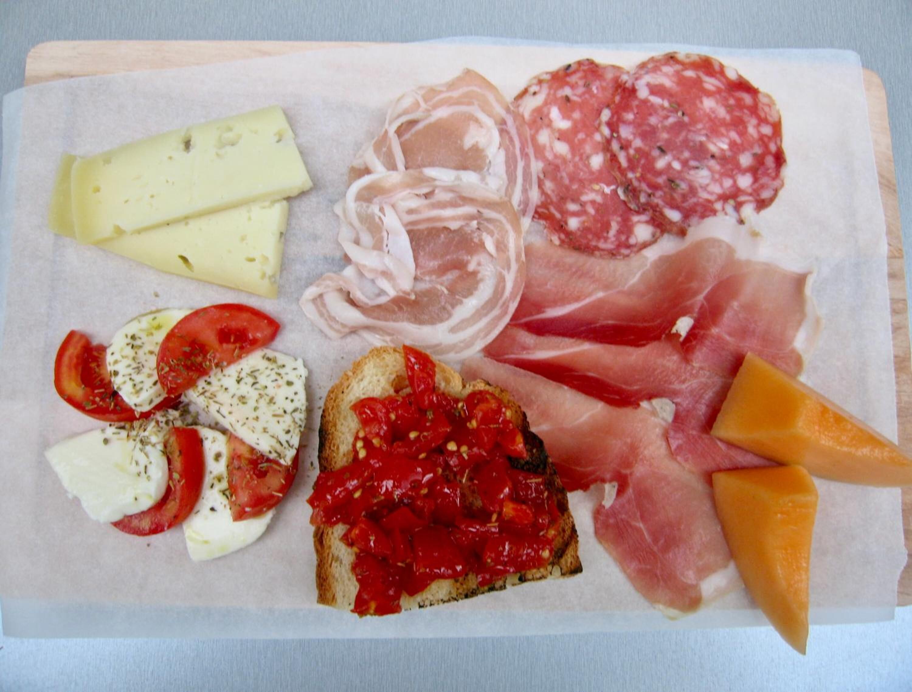 A charcuterie board with various meats, cheeses, and a slice of bread with tomato and herb topping.