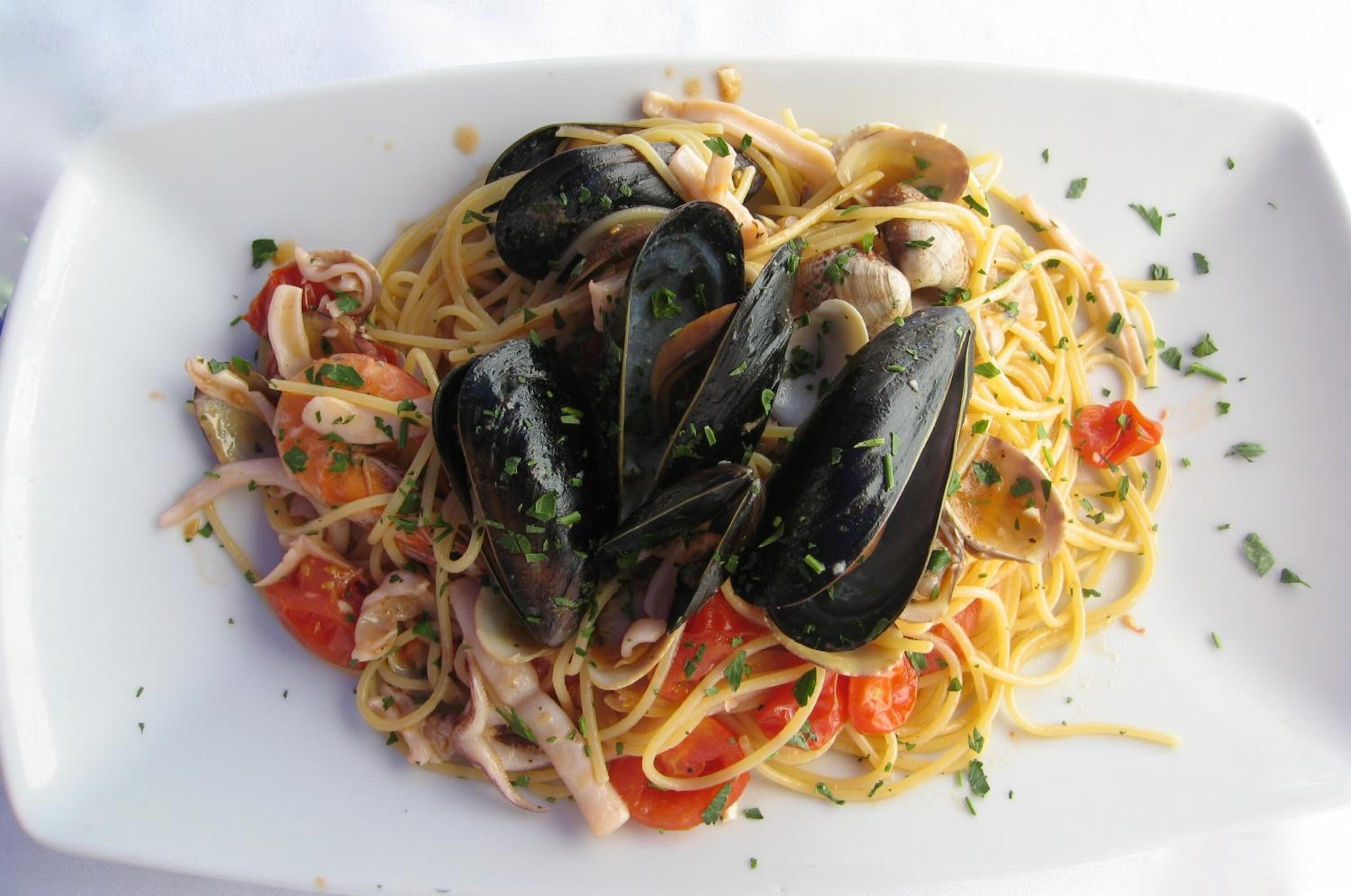 A plate of pasta with mussels, tomatoes, and herbs.