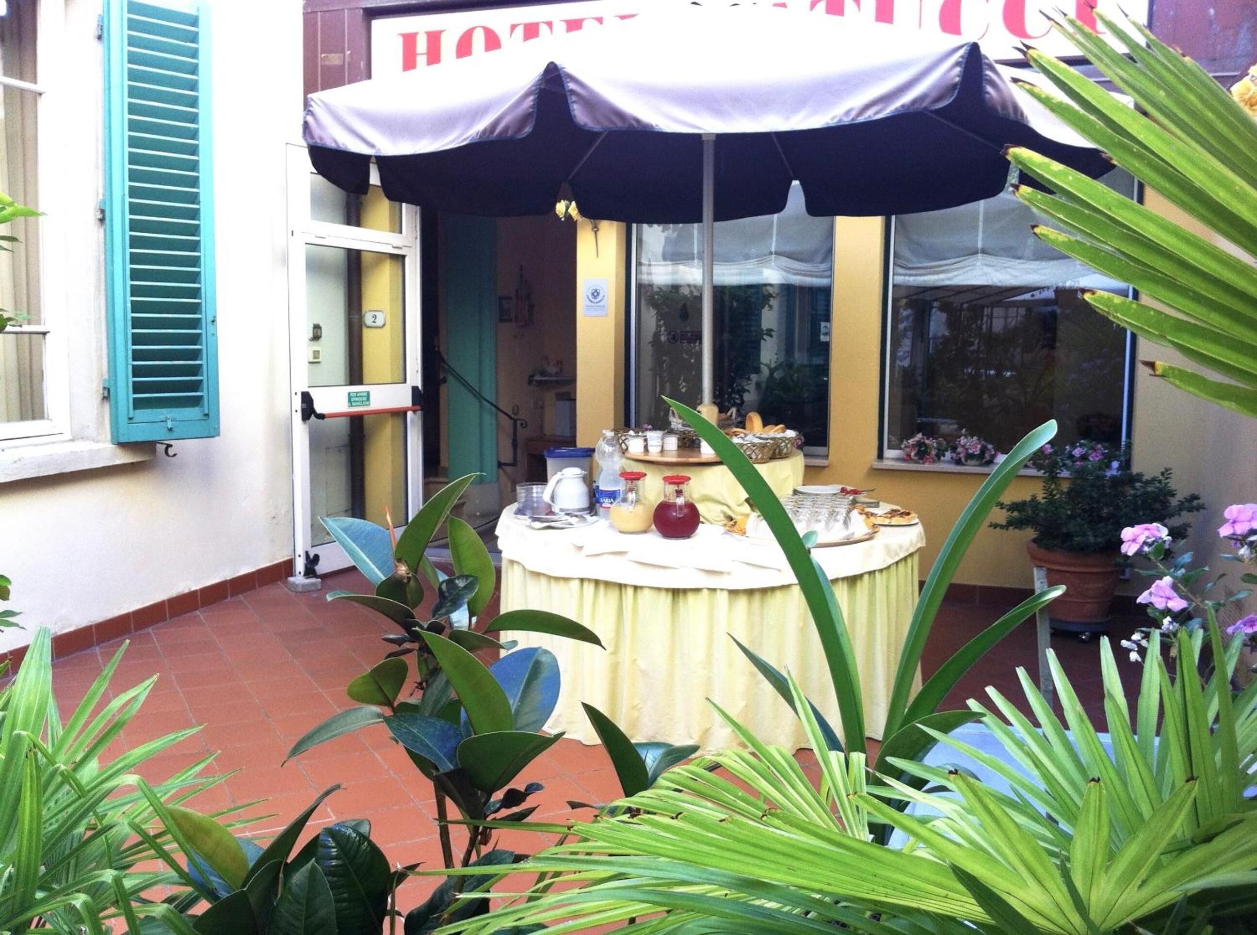 Patio d'albergo con tavolo rotondo apparecchiato per la colazione, sedute all'aperto e vasi di piante.