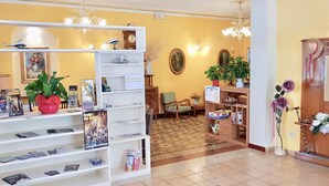 Un hall d'hôtel comprenant un comptoir d'accueil, des étagères remplies de magazines et de livres, une horloge et un arrangement floral.
