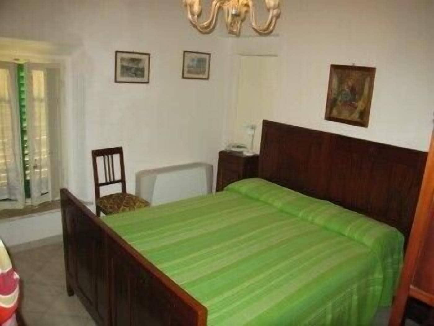 Ein Schlafzimmer mit einem hölzernen Bett, einem Sessel, einem Schreibtisch und einem Fenster mit Vorhängen.