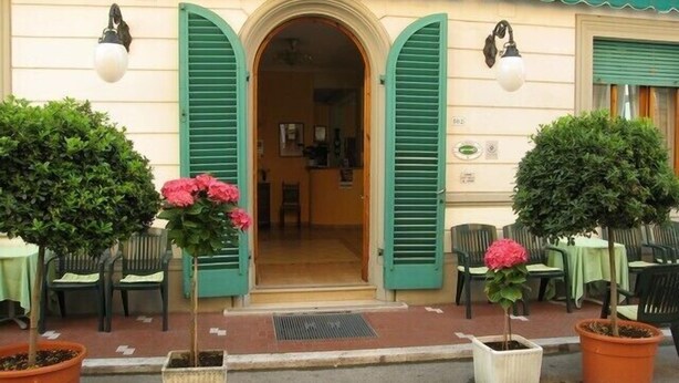 Un bâtiment doté d’un auvent vert, d’une porte avec des volets verts et de plantes en pot ornées de fleurs roses.