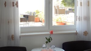 A room with a table set for two, a window with a view of the outside, and a potted plant on the windowsill. - Dubrovnik Apartments Kovacec (Dubrovnik)