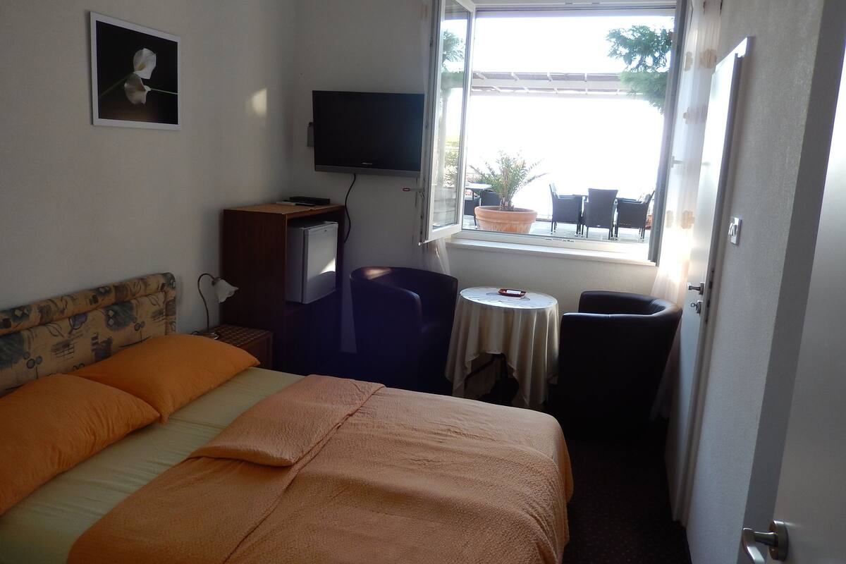 Habitación de hotel con cama, escritorio, televisión, ventana y vista al exterior, además de una pequeña mesa.
