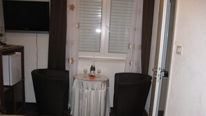 A hotel room with a bed, a small table with a bottle and glasses, two chairs, a TV, and a window with curtains. - Dubrovnik Apartments Kovacec (Dubrovnik)