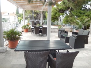 En udendørs patio med et bord og stole, omgivet af krukker med planter og et pergola.
