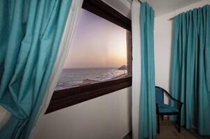Una habitación con vista al mar a través de una ventana, una silla y cortinas color turquesa.