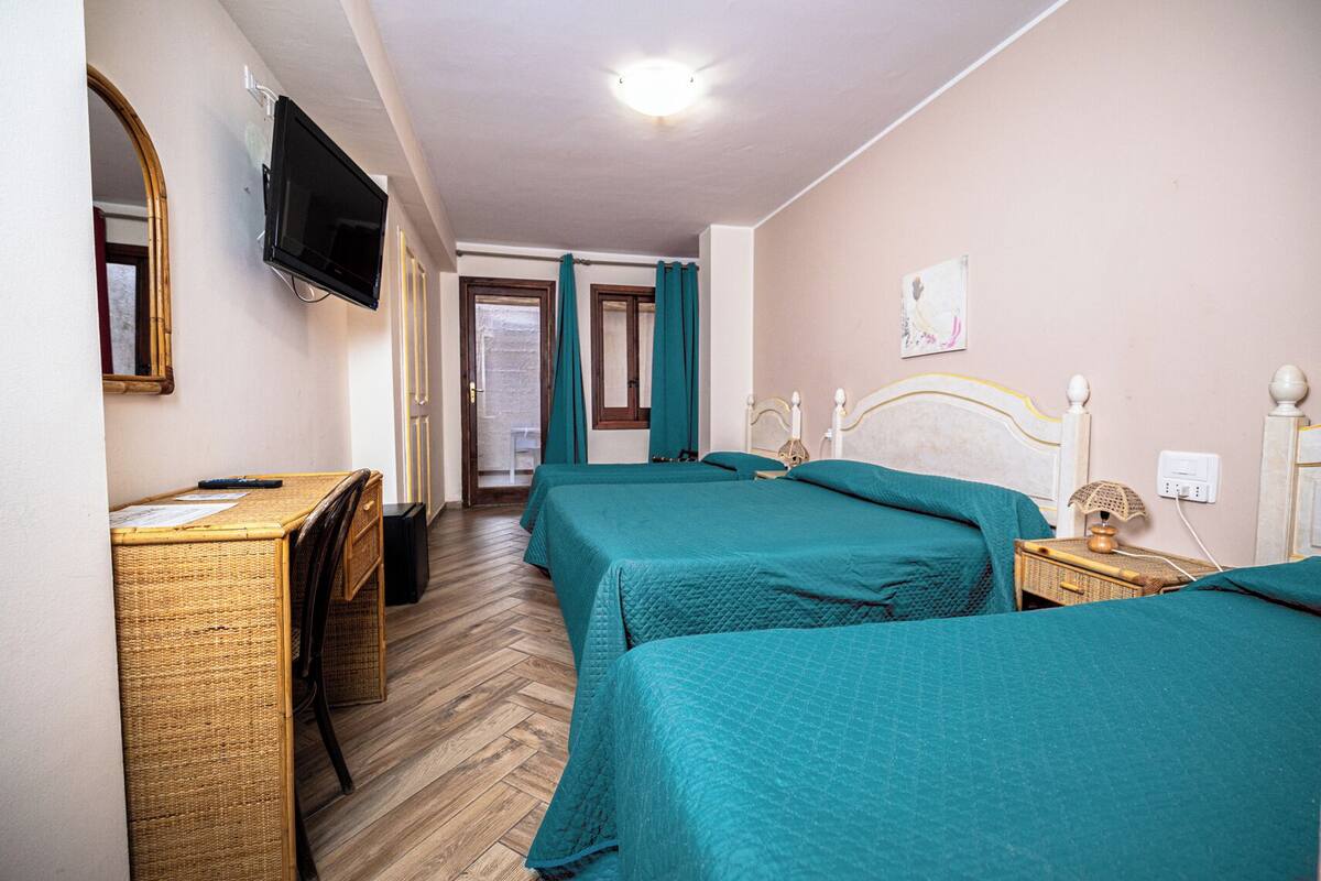 A hotel room with two beds, a desk, a television, and a door leading to a balcony.