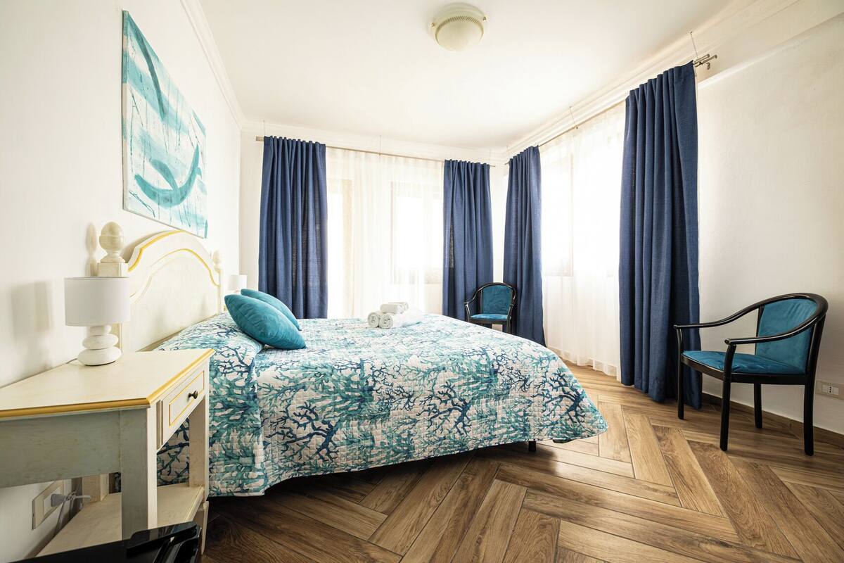 A bedroom with a bed, a chair, a desk, and a painting on the wall.