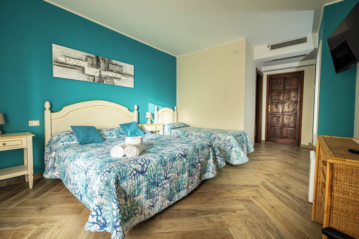 A bedroom with two beds, a wooden floor, a teal wall, and a painting.