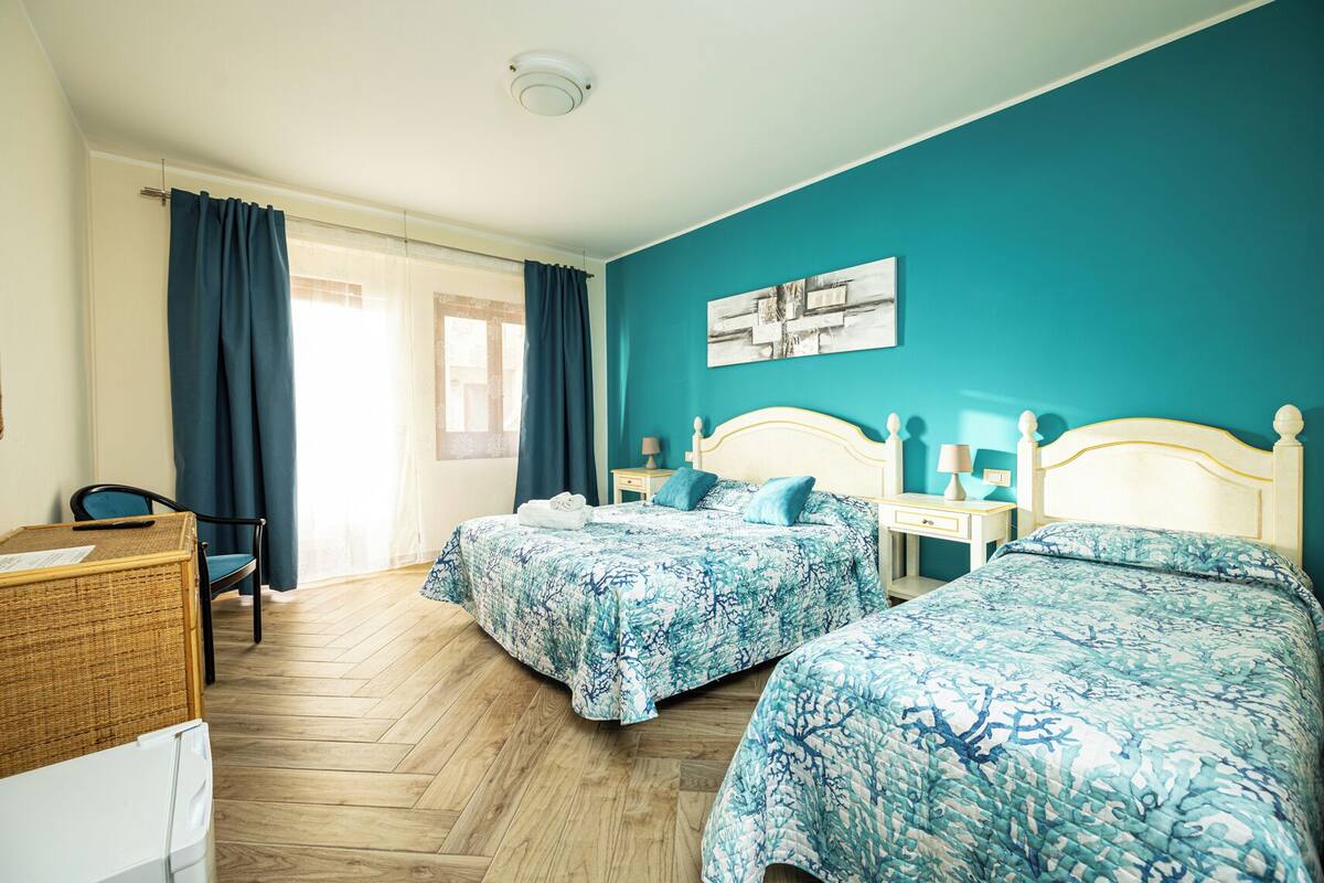 A hotel room with two beds, a desk, a chair, and a window with curtains.