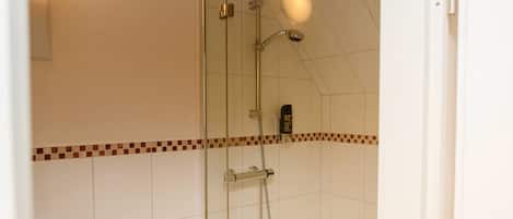 A shower with glass doors, a tiled wall with a decorative border, and a visible water heater.