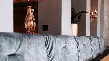 A modern interior with a grey upholstered bench, wooden tables, and a chandelier.