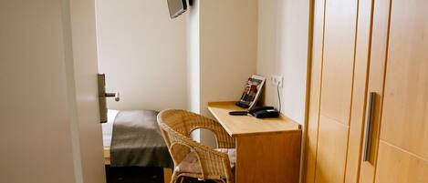 A small room with a bed, a wicker chair, a desk with a phone, and a magazine on the wall.