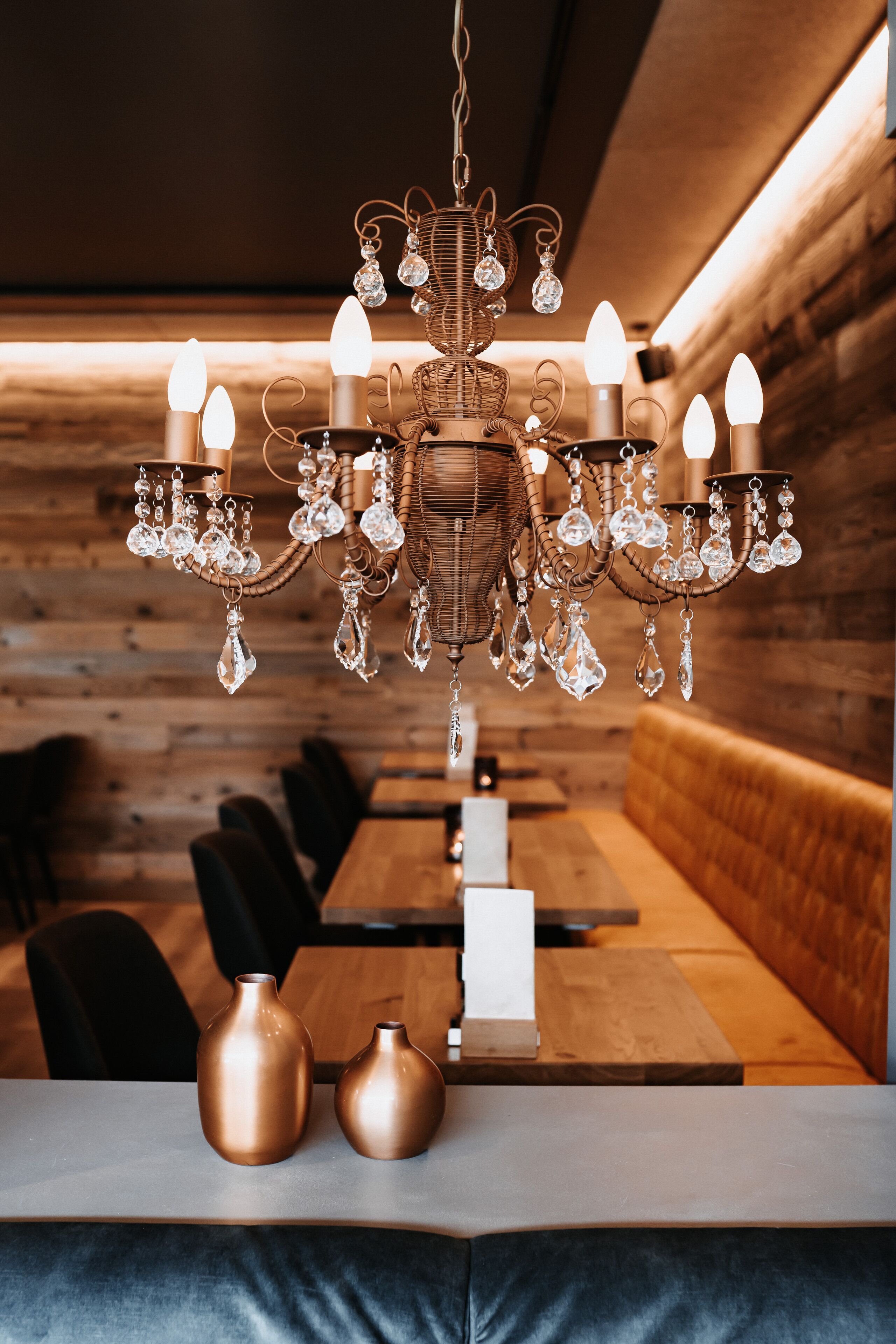 A chandelier with crystal decorations hanging above a wooden dining table with two vases.