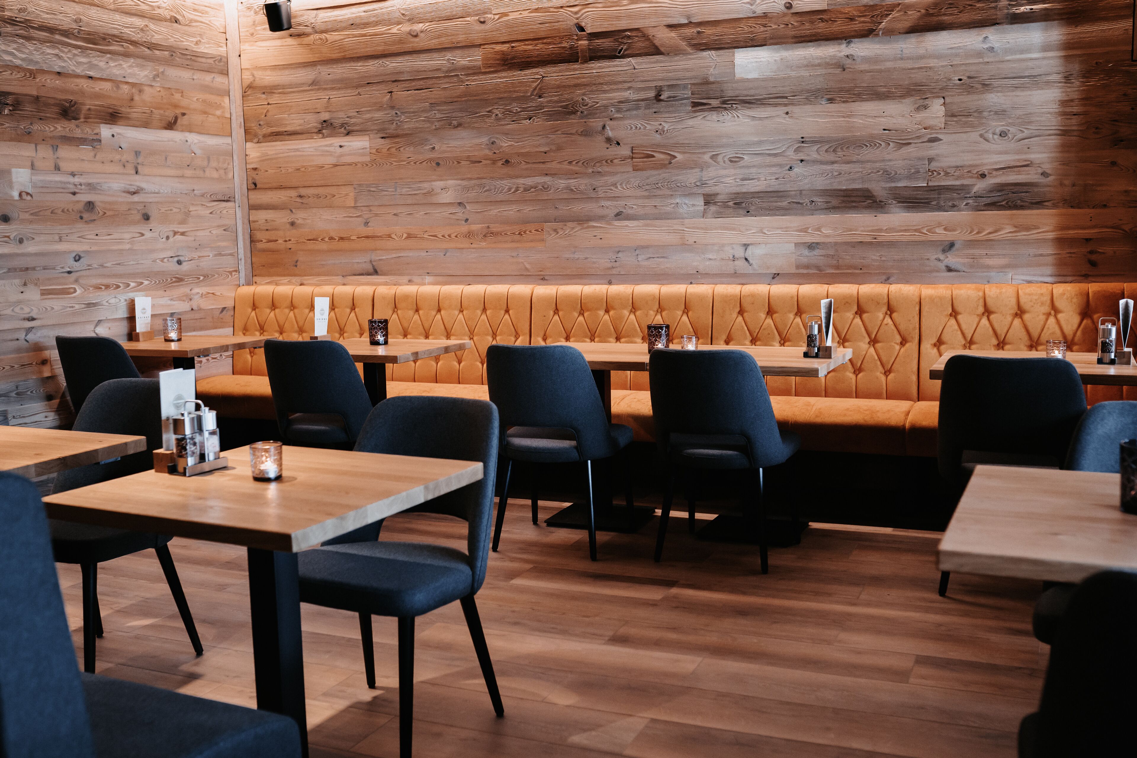 A restaurant with wooden walls, a cushioned bench, and tables with chairs.