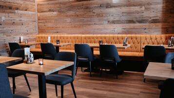 A restaurant with wooden walls, a cushioned bench, and tables with chairs.