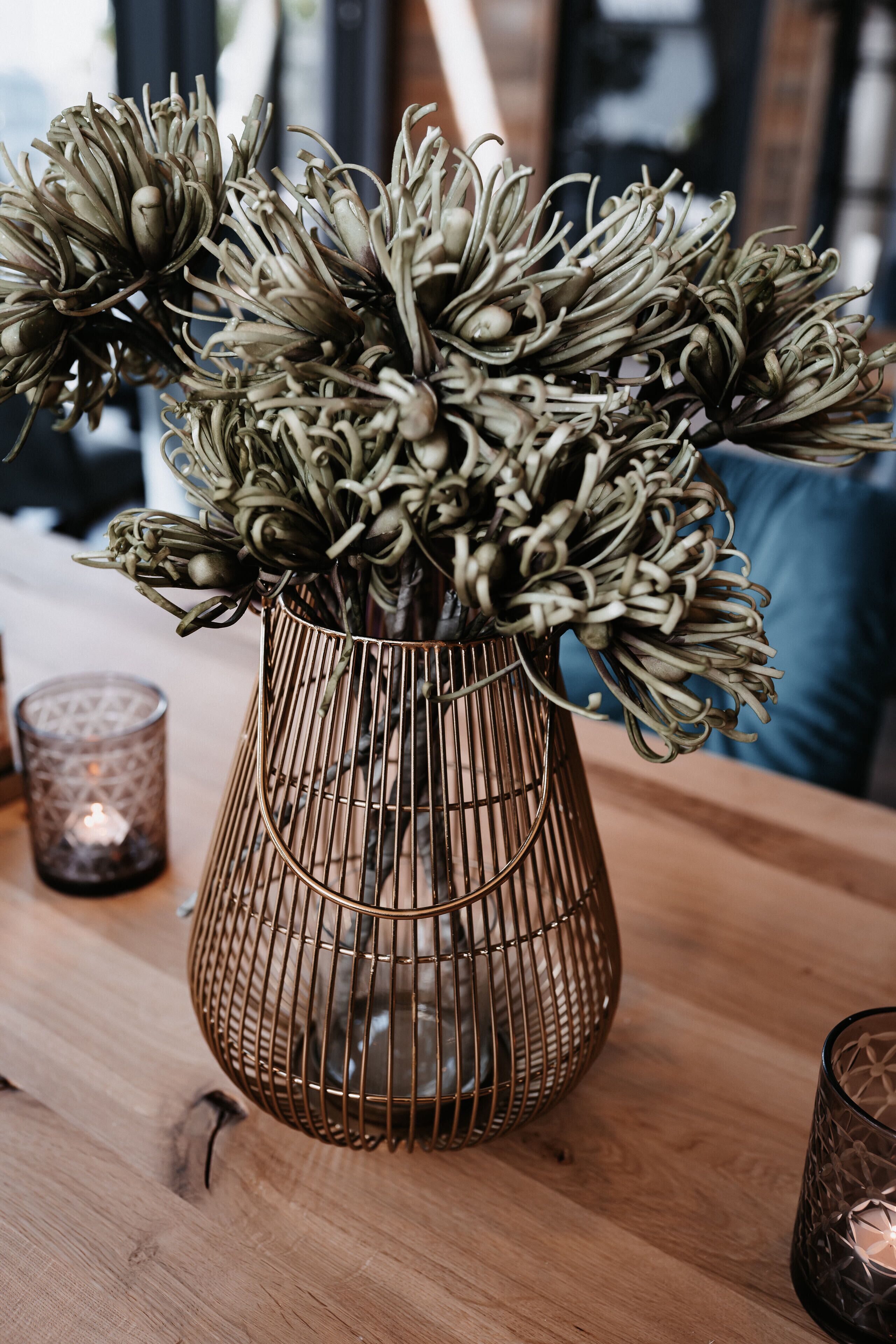 A metal vase with dried flowers on a wooden table.