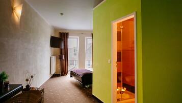 A narrow hallway with a bed, a television, and a small table with a plant.