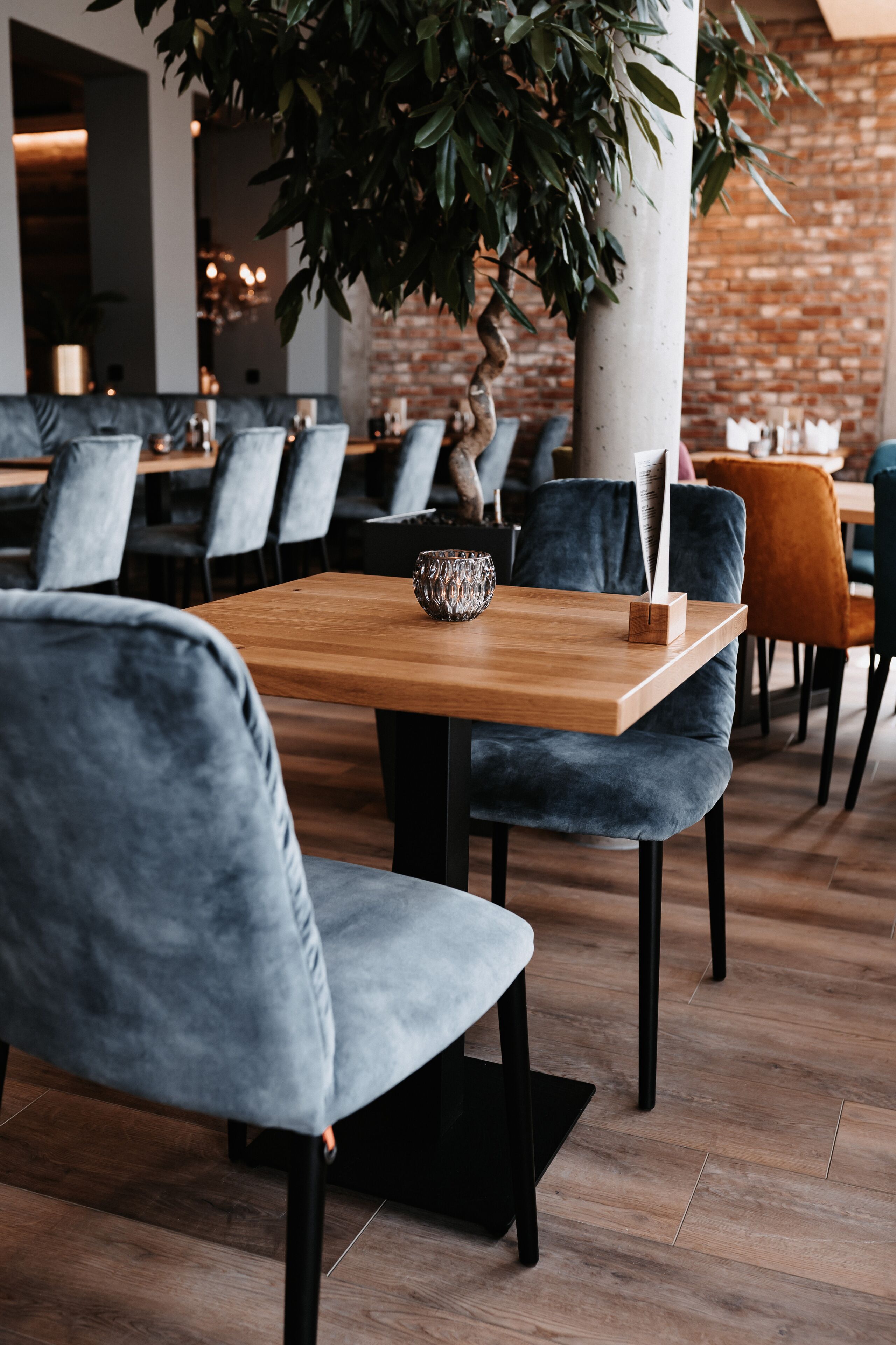 Interno di un ristorante con un tavolo in legno, sedie rivestite di grigio e una parete in mattoni sullo sfondo.