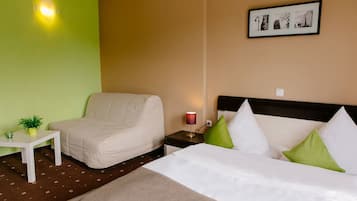 Een hotelkamer met een bed, een stoel, een nachtkastje met een lamp, een bijzettafeltje met een plant en een aan de muur hangend schilderij.