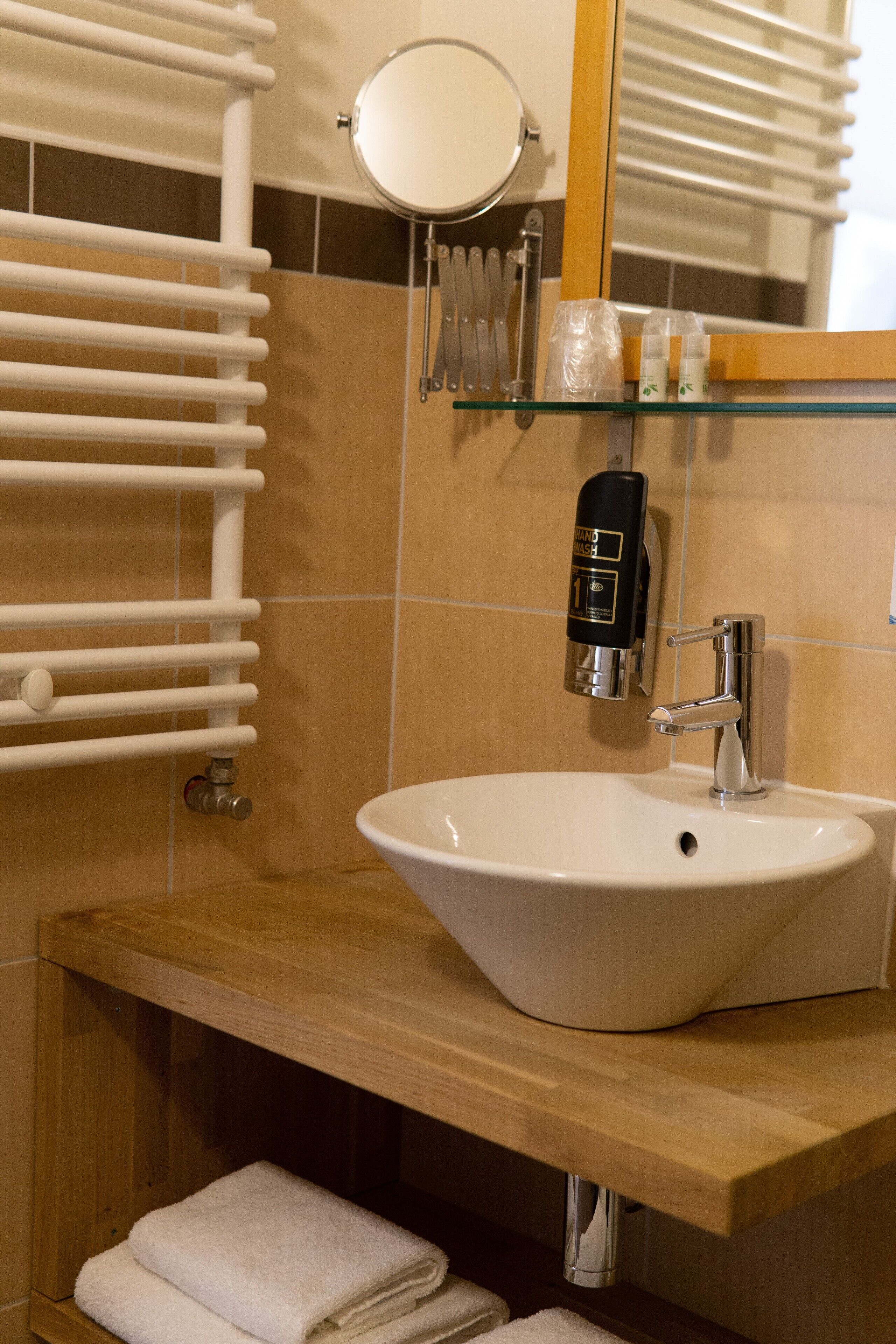 A bathroom with a white sink, a glass soap dispenser, a towel rack, and a mirror.