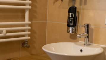 A bathroom with a white sink, a glass soap dispenser, a towel rack, and a mirror.