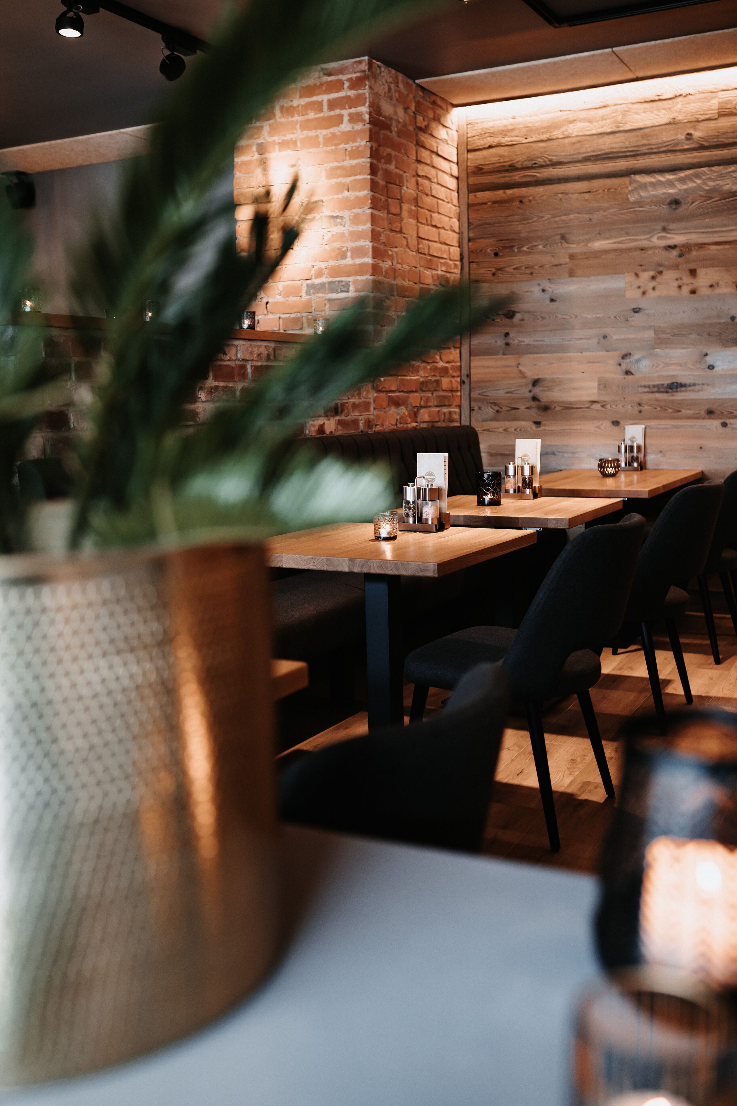Un restaurant avec des tables et des chaises en bois, un mur en briques et une plante en pot.