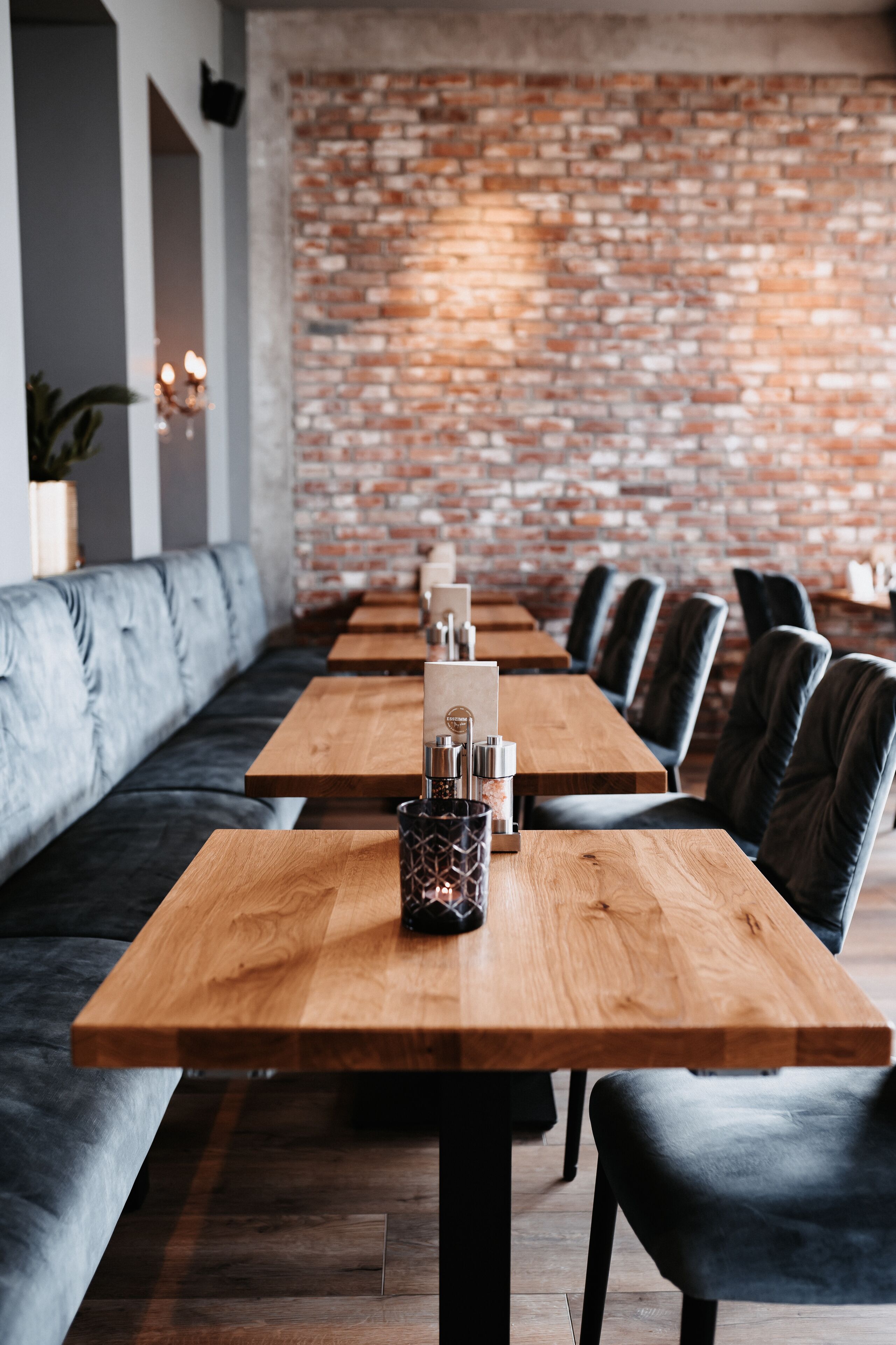 A long wooden table with a candle holder in the center, set against a brick wall.