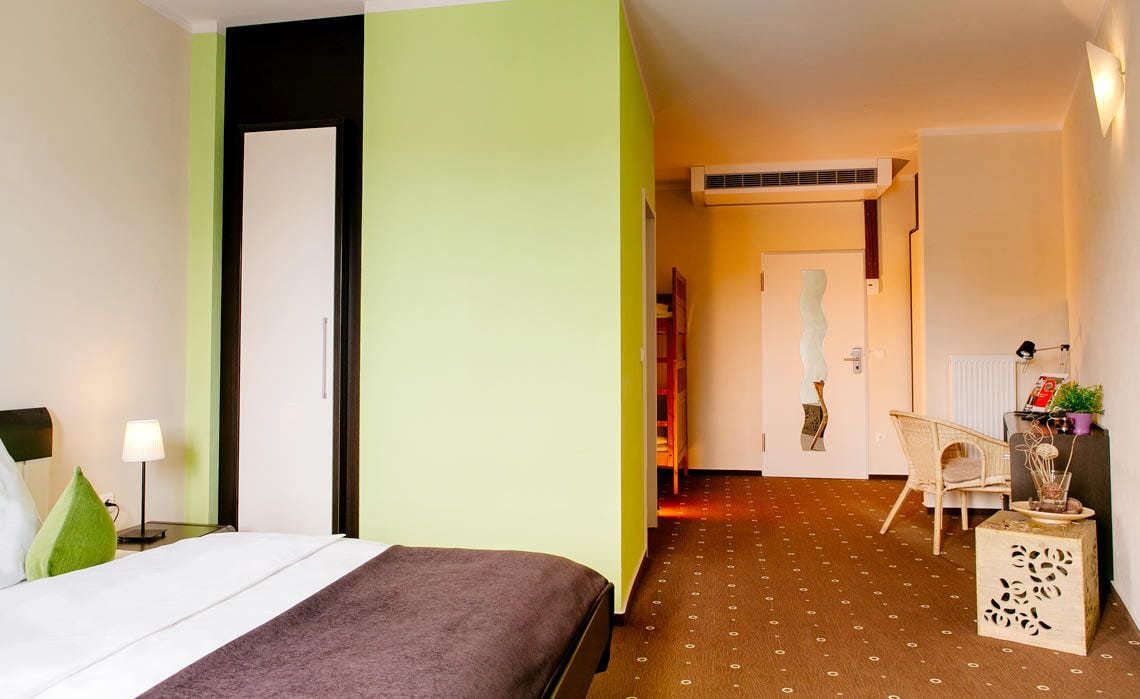 Una habitación de hotel con una cama, una mesita de noche, una lámpara, una silla y una pequeña mesa con una planta.