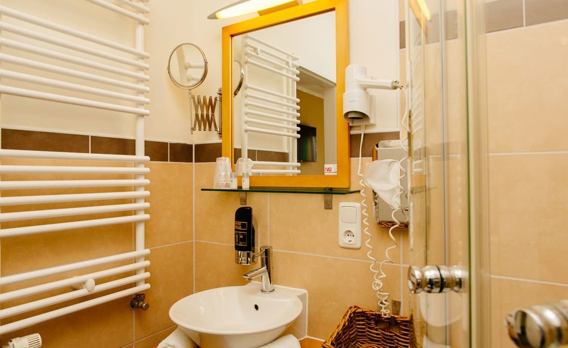 Un baño con un lavabo blanco, un estante de vidrio con artículos de aseo, un espejo con marco amarillo y un perchero para toallas.