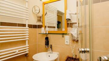 Un baño con un lavabo blanco, un estante de vidrio con artículos de aseo, un espejo con marco amarillo y un perchero para toallas.