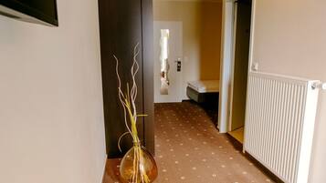 A hallway with a vase of branches, a radiator, and a bed in the distance.