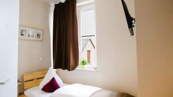 Een kleine kamer met een enkel bed, een raam, een tv aan de muur en een ingelijst schilderij.