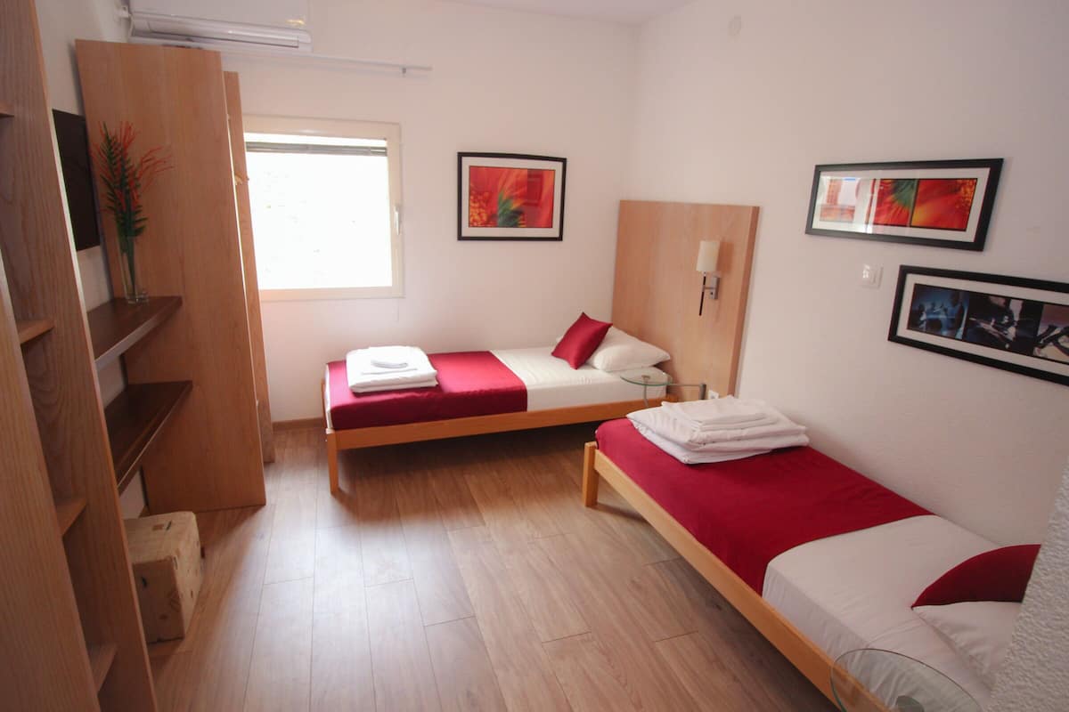 Habitación de hotel con dos camas individuales, suelo de madera, ventana y cuadros en las paredes.