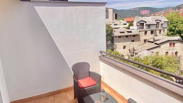 A balcony with a tiled floor, a wicker chair with a red cushion, and a small table with a candle.