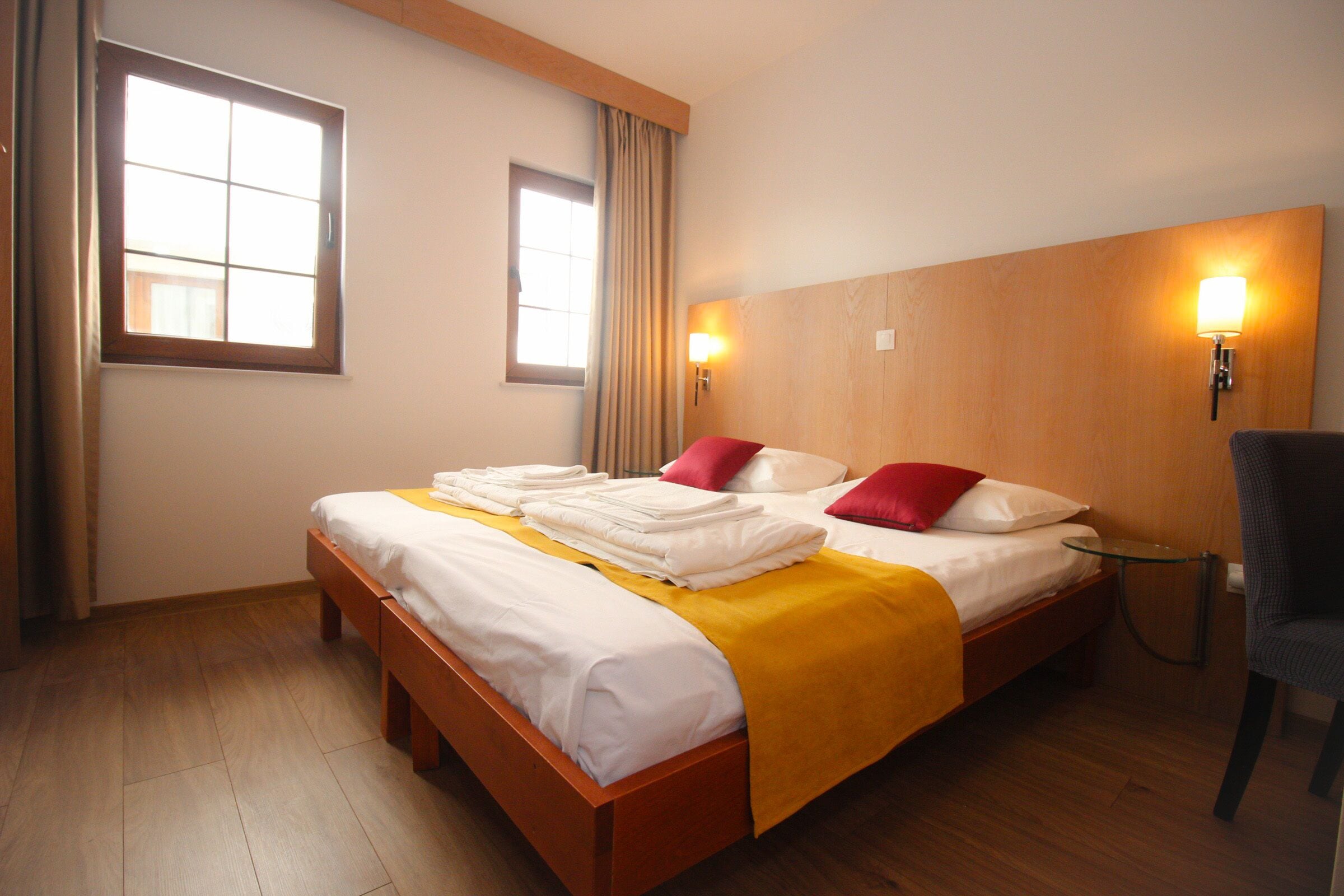 A hotel room with a wooden bed, two bedside lamps, a small table, and a chair.