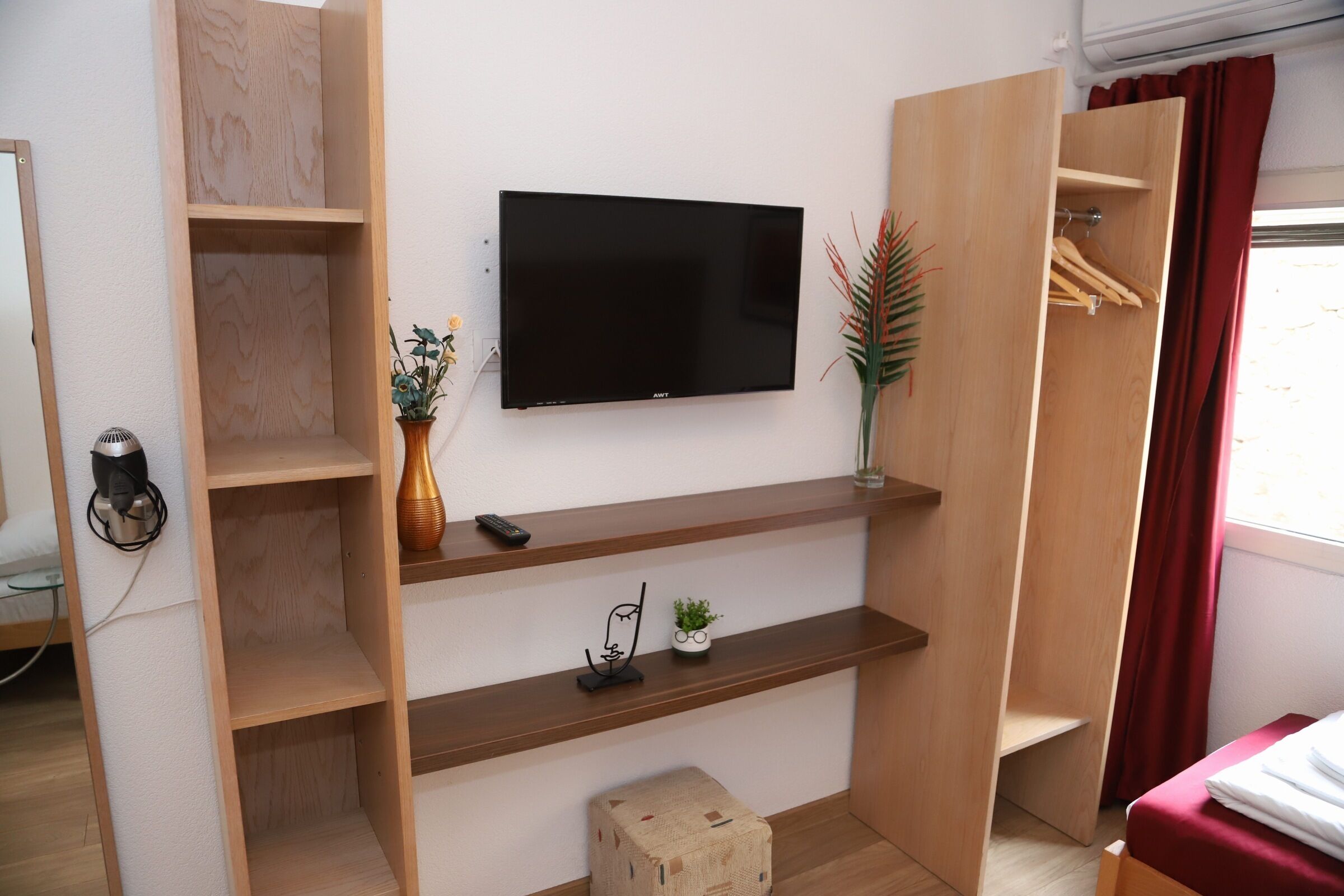 A room with a mounted TV, wooden shelves, a small plant, and a red curtain.